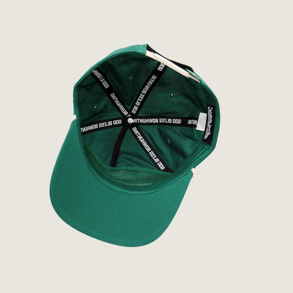 The back view of a green baseball cap with black adjustable straps featuring white text, photographed on a light beige background.